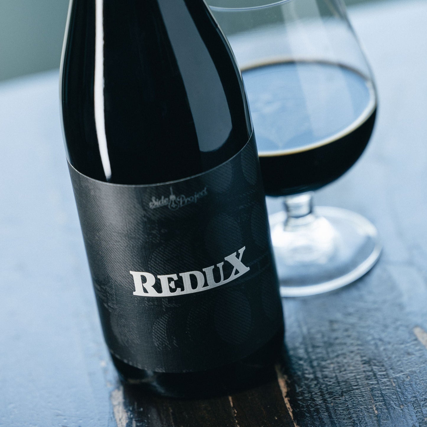 Bottle of Redux stout beer with a glass on a wooden surface