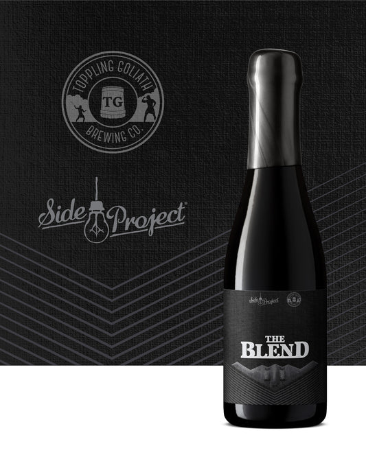 Black beer bottle labeled 'The Blend' with Topping Goliath Brewing Co. and Side Project logos on a dark background.