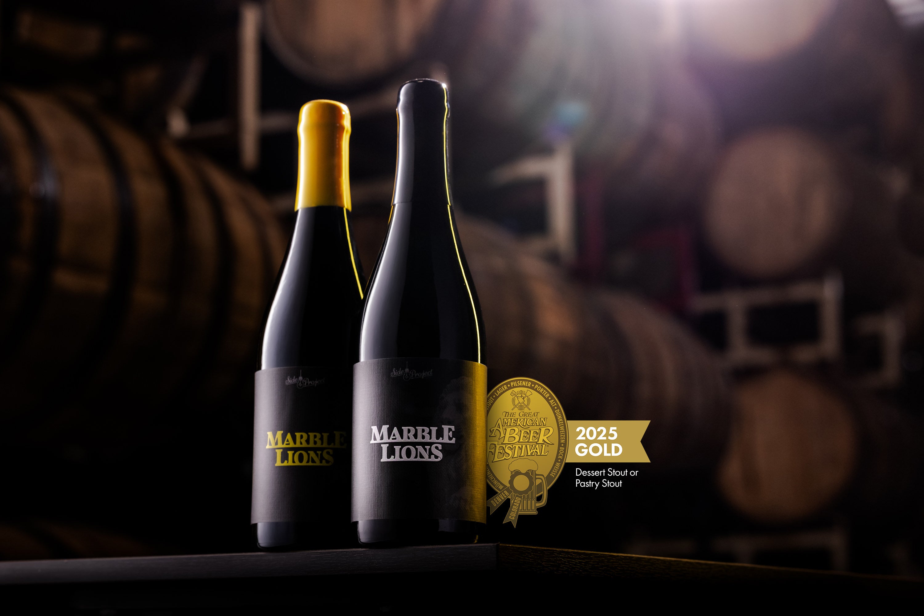 Two bottles of Marble Lions Barrel Aged Imperial Stout Beer with a gold medal in front of whiskey barrels.