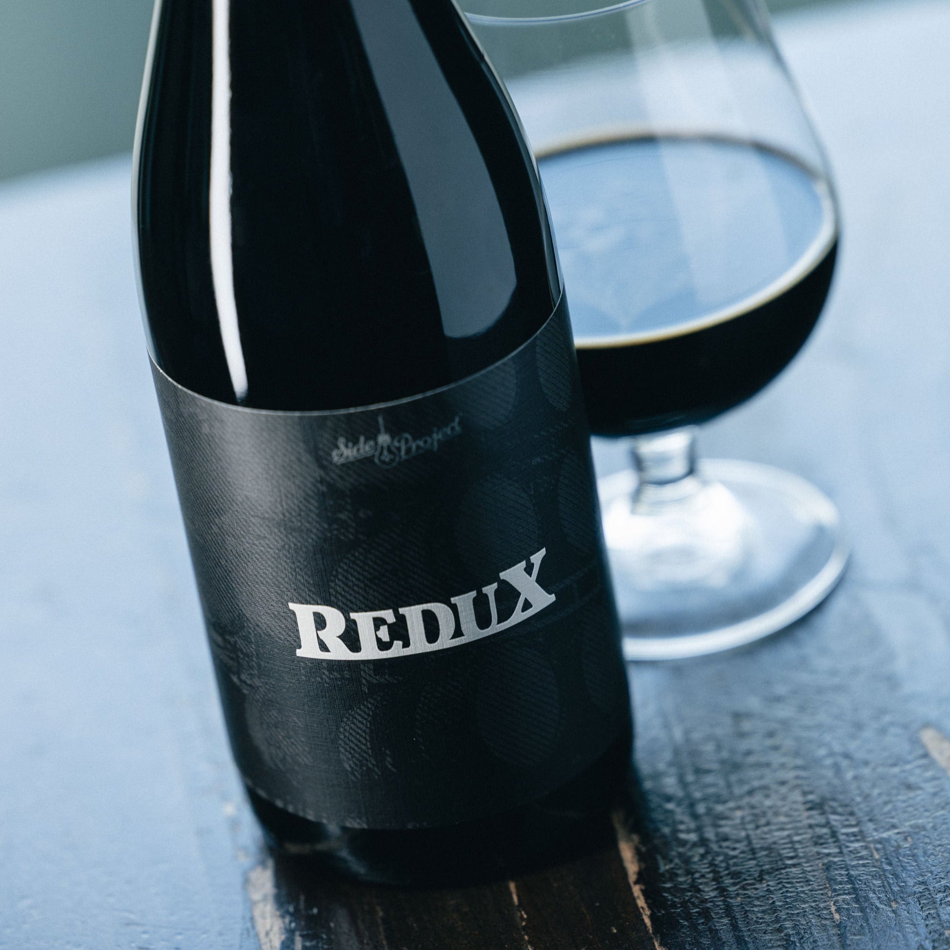 Bottle of Redux stout beer with a glass on a wooden surface