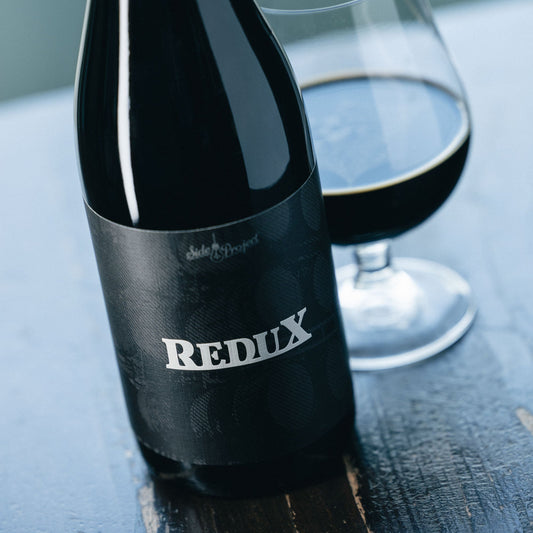 Bottle of Redux stout beer with a glass on a wooden surface